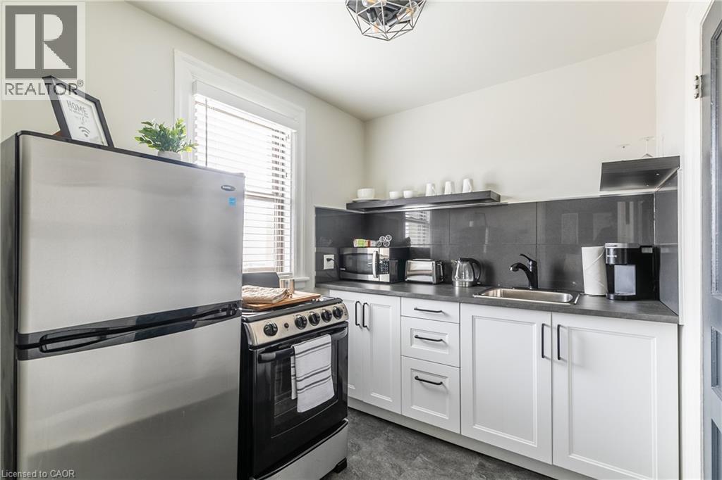 Kitchen with stainless steel appliances, dark countertops, white cabinetry, backsplash, and open shelves - 14 Duke Street, Hamilton, ON - Indoor Photo Showing Kitchen