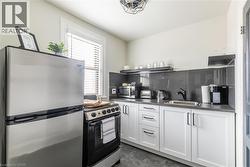 Kitchen with stainless steel appliances, dark countertops, white cabinetry, backsplash, and open shelves -