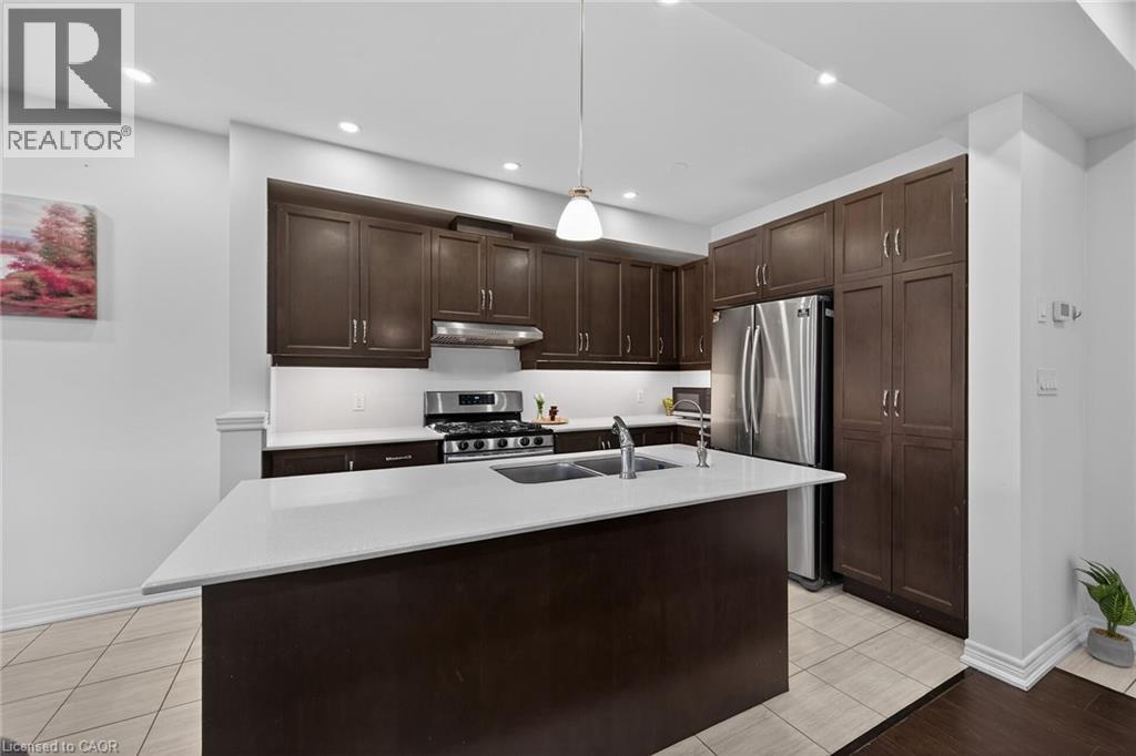 Kitchen with dark wood finish cabinetry, stainless steel appliances, a kitchen island with sink, light stone countertops, and hanging light fixtures - 80 Severino Circle, Smithville, ON - Indoor Photo Showing Kitchen With Double Sink