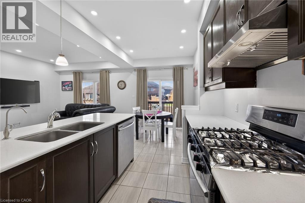 Kitchen with stainless steel appliances, dark wood finish cabinets, open floor plan, light stone countertops, and decorative light fixtures - 80 Severino Circle, Smithville, ON - Indoor Photo Showing Kitchen With Double Sink With Upgraded Kitchen