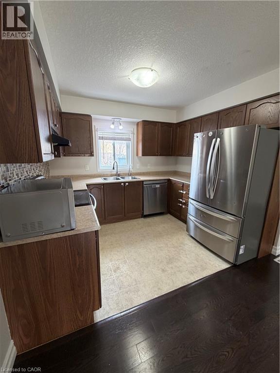 Kitchen featuring stainless steel appliances, dark wood finish cabinets, light countertops, light wood finished floors, and a textured ceiling - 45 Brookfield Crescent, Kitchener, ON - Indoor Photo Showing Kitchen With Double Sink