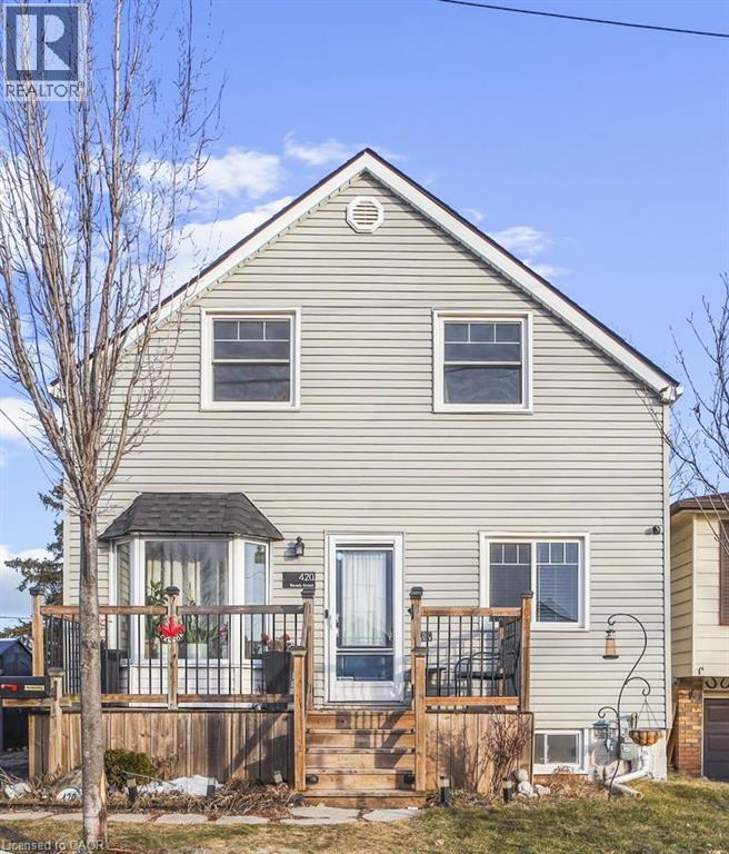 The property features light-colored horizontal siding and a prominent front deck with wooden stairs and black railings - 420 Waverly Street, Hamilton, ON - Outdoor With Deck Patio Veranda