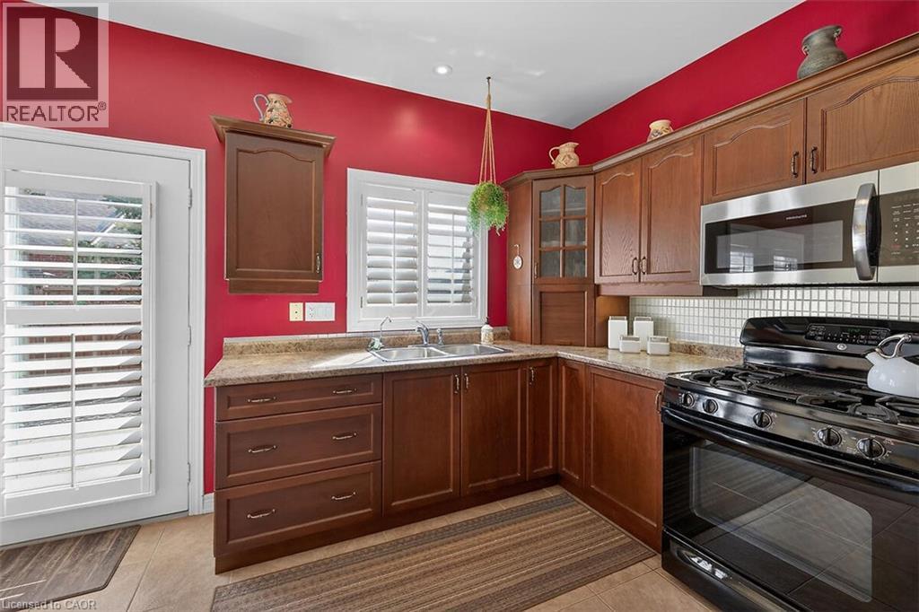 Kitchen with black range with gas stovetop, stainless steel microwave, glass fronted cabinets, tasteful backsplash, and light tile patterned floors - 48 Hallmark Trail, Hamilton, ON - Indoor Photo Showing Kitchen With Double Sink
