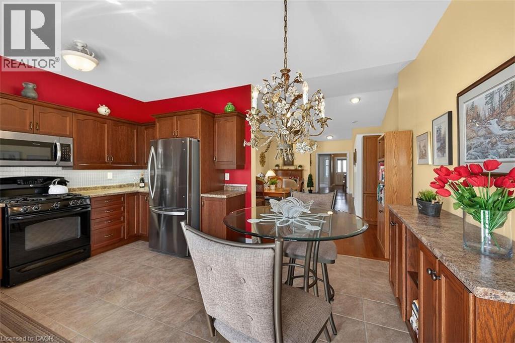 Kitchen with stainless steel appliances, light stone counters, a chandelier, backsplash, and light tile patterned floors - 48 Hallmark Trail, Hamilton, ON - Indoor Photo Showing Kitchen