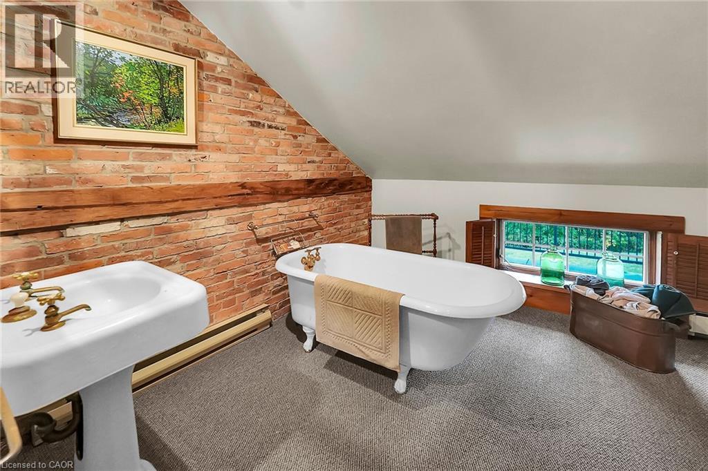 Full bath with brick wall, a freestanding tub, baseboard heating, lofted ceiling, and carpet - 2432 Seburn Road, Fonthill, ON - Indoor Photo Showing Bathroom