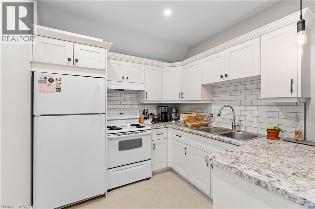 Kitchen featuring white appliances, decorative backsplash, white cabinets, and light stone countertops - 58 Hohner Avenue, Kitchener, ON - Indoor Photo Showing Kitchen With Double Sink