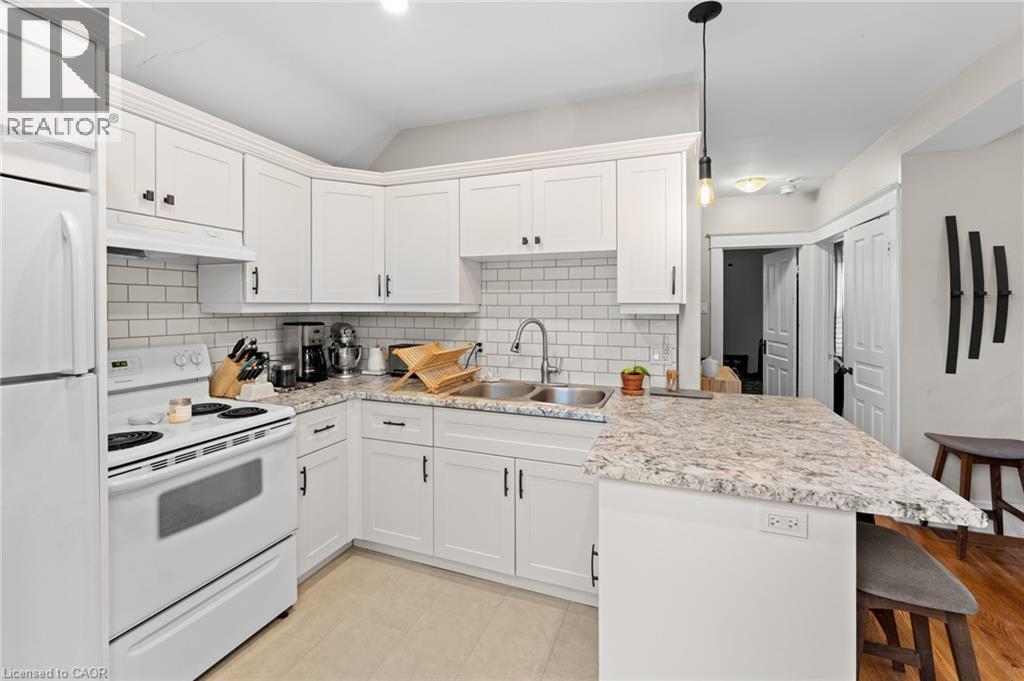 Kitchen featuring white appliances, a peninsula, white cabinetry, and a kitchen bar - 58 Hohner Avenue, Kitchener, ON - Indoor Photo Showing Kitchen
