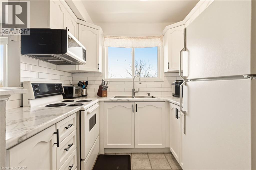 Kitchen featuring white appliances, white cabinets, and light countertops, double sinks overlooking rear - 2373 E King Street E Unit# 45, Hamilton, ON - Indoor Photo Showing Kitchen With Double Sink