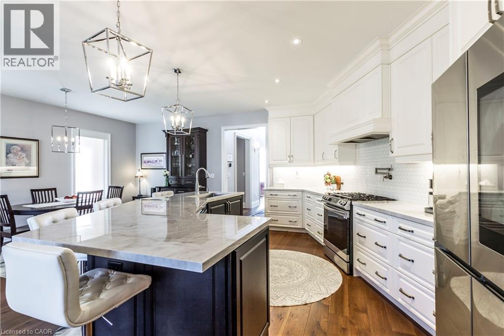 Two tone kitchen featuring stainless steel appliances, two tone color scheme, dark wood finished floors, light stone countertops, and a breakfast bar area - 72 Pond View Gate, Waterdown, ON - Indoor