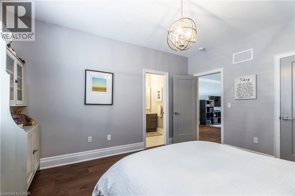 Bedroom with dark wood finished floors, a chandelier, and connected bathroom - 72 Pond View Gate, Waterdown, ON - Indoor Photo Showing Bedroom