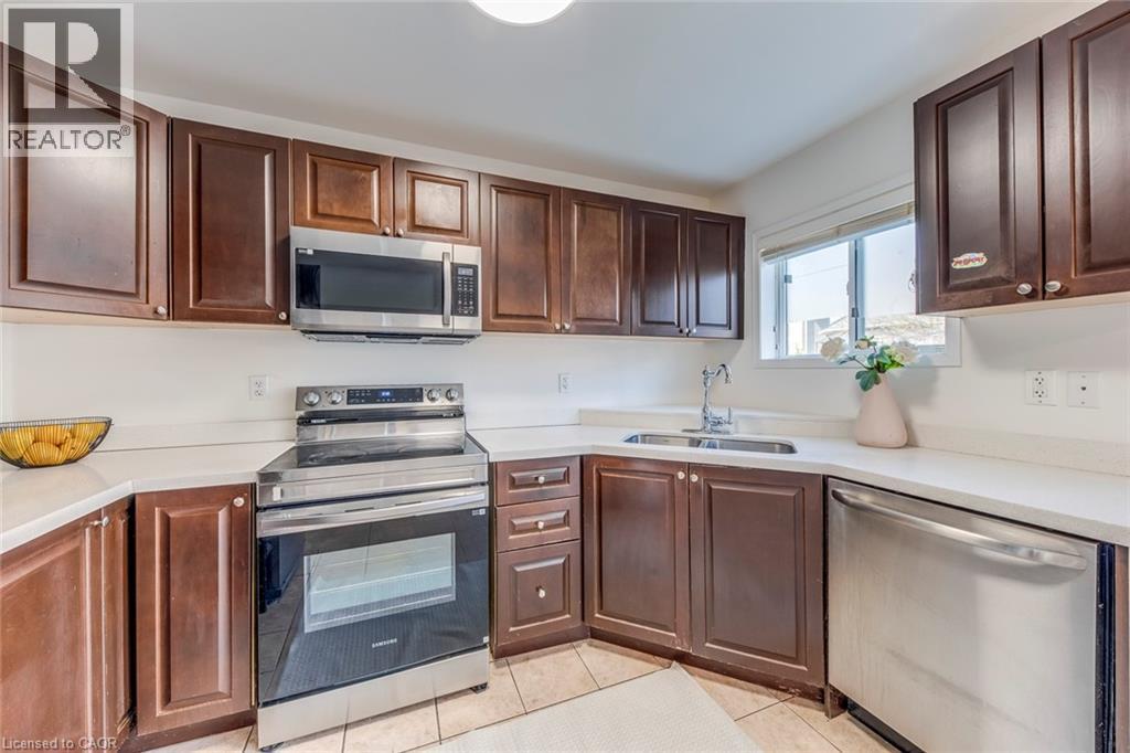 Kitchen featuring stainless steel appliances, dark wood finish cabinetry, and light tile patterned floors - 5811 Page Crescent, Burlington, ON - Indoor Photo Showing Kitchen With Double Sink