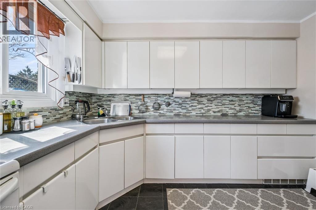 Kitchen with white cabinets, backsplash, and dark tile patterned flooring - 55 Ralgreen Crescent, Kitchener, ON - Indoor Photo Showing Kitchen With Double Sink