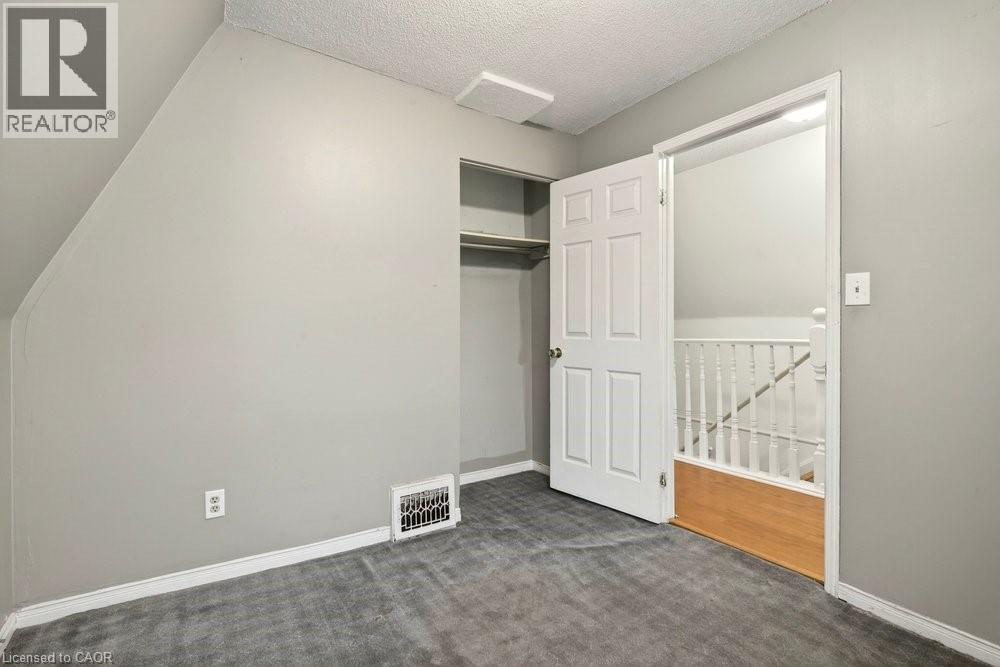 Unfurnished bedroom with dark carpet, a textured ceiling, and a closet - 23 Frederick Avenue, Hamilton, ON - Indoor Photo Showing Other Room