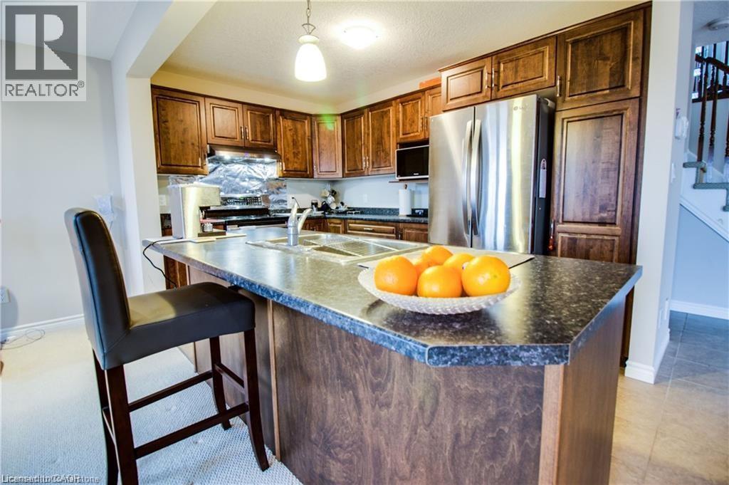 Kitchen featuring pendant lighting, a kitchen island with sink, a kitchen breakfast bar, sink, and stainless steel appliances - 101 Robert Simone Way, Ayr, ON - Indoor Photo Showing Kitchen With Double Sink