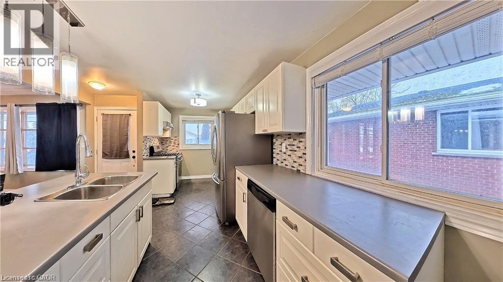 Kitchen featuring white cabinets, stainless steel appliances, light countertops, dark tile patterned flooring, and hanging light fixtures - 61 Bosworth Crescent Unit# Upper, Kitchener, ON - Indoor Photo Showing Kitchen With Double Sink