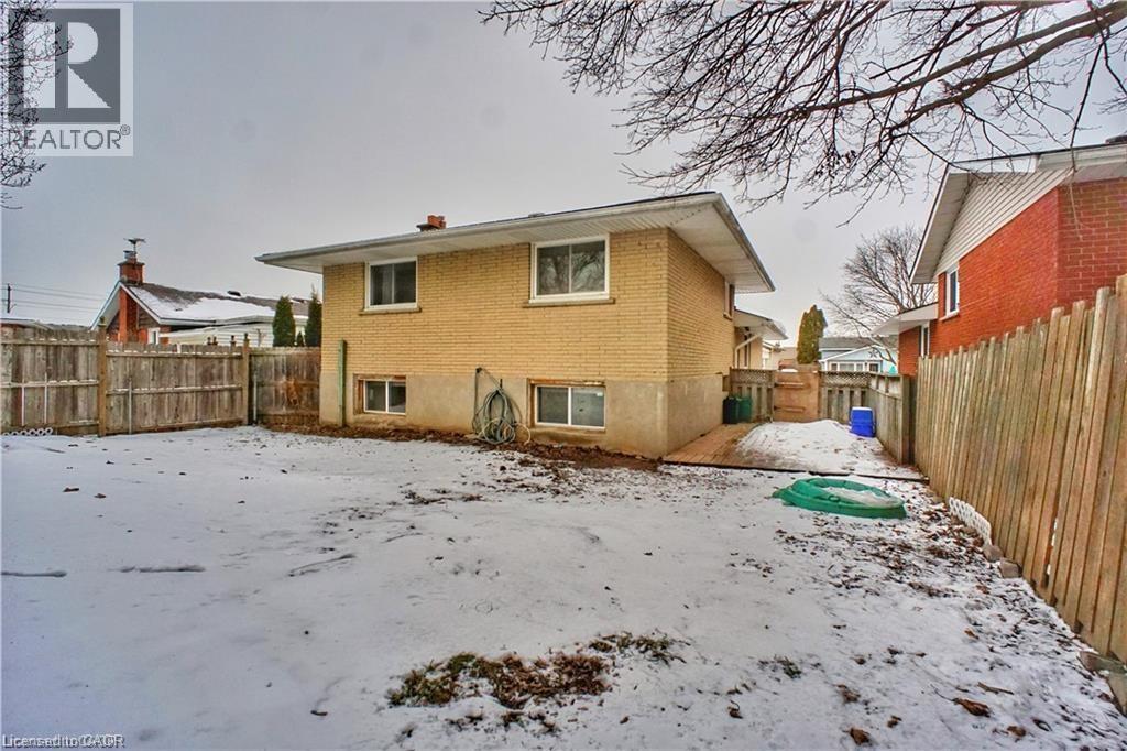 Snow covered back of property featuring a fenced backyard, brick siding, and a chimney - 61 Bosworth Crescent Unit# Upper, Kitchener, ON - Outdoor With Exterior