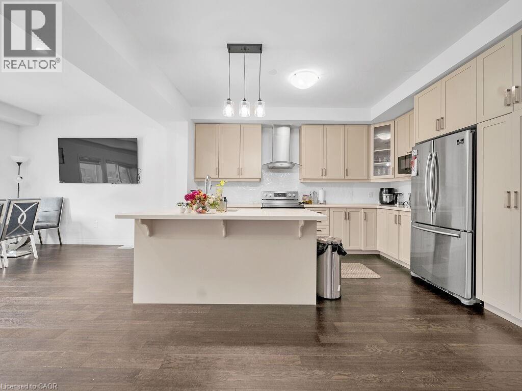 Kitchen with cream cabinets, stainless steel appliances, dark wood-style floors, and a kitchen bar - 30 Times Square Boulevard, Hamilton, ON - Indoor Photo Showing Kitchen
