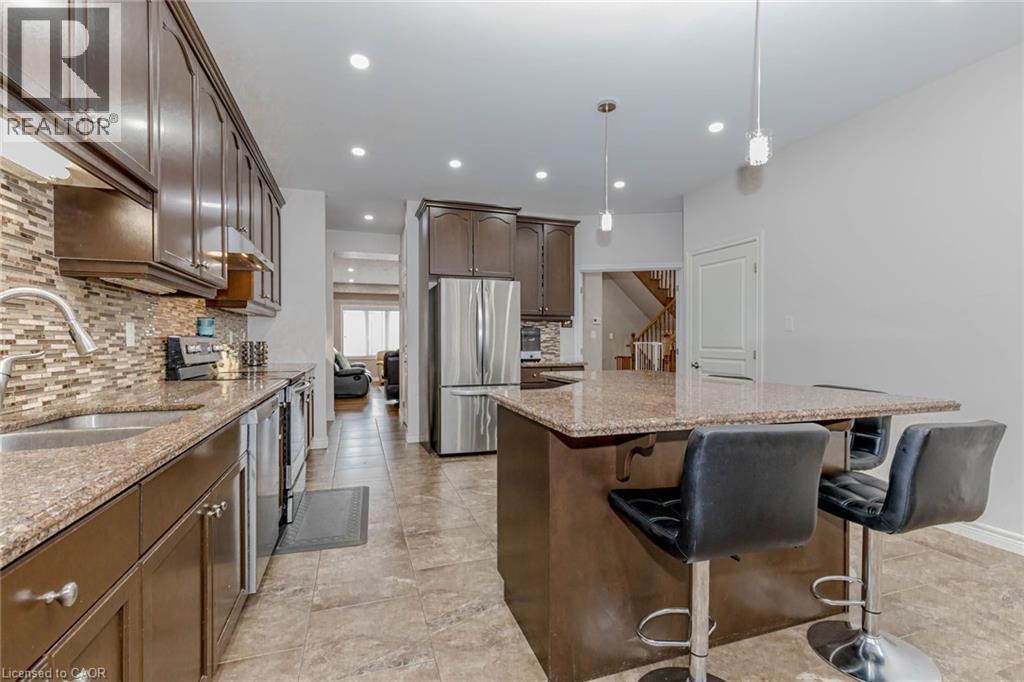 Kitchen with light stone counters, stainless steel appliances, a kitchen island, a kitchen breakfast bar, and dark wood finish cabinets - 2 Doon Creek Street, Kitchener, ON - Indoor Photo Showing Kitchen With Double Sink With Upgraded Kitchen