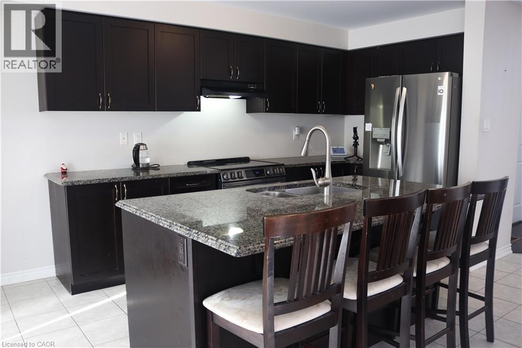 Kitchen with stainless steel appliances, light tile patterned flooring, a center island with sink, dark stone counters, and a kitchen breakfast bar - 31 Sofitel Drive, Kitchener, ON - Indoor Photo Showing Kitchen With Double Sink With Upgraded Kitchen