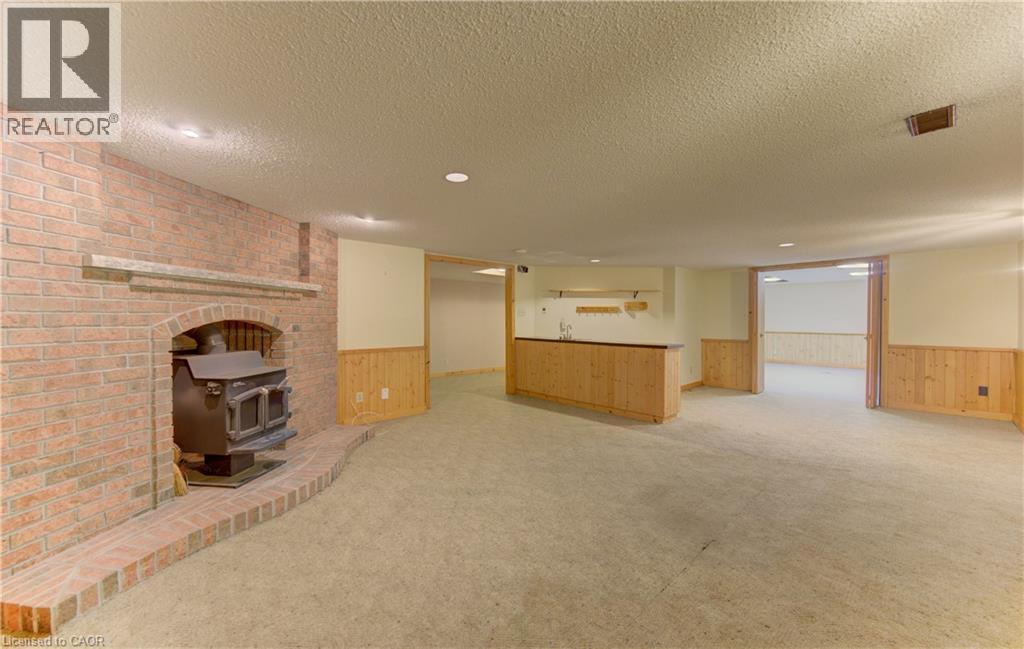 Unfurnished living room featuring a wainscoted wall, wood walls, light colored carpet, a wood stove, and bar area - 190 Silvercrest Drive, Waterloo, ON - Indoor