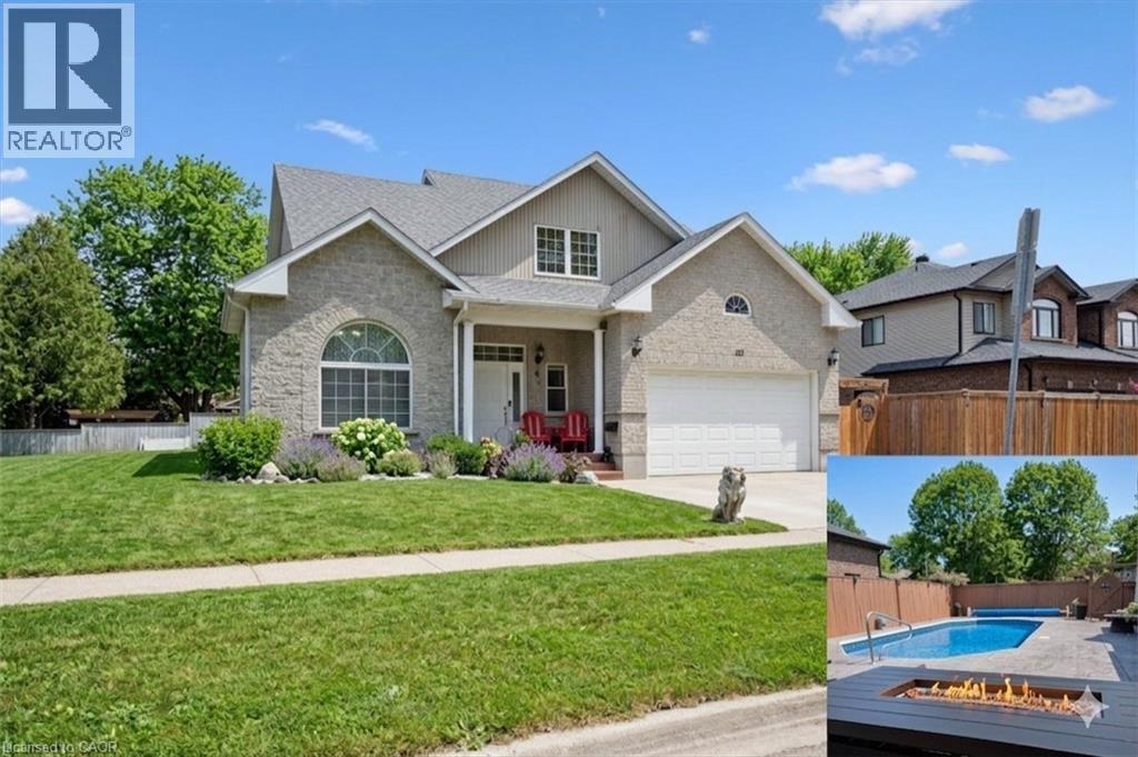 View of front of property with concrete driveway, covered porch, stone siding, and an attached garage. Digitally Enhanced – Lawn and sky edited for seasonal representation. - 122 Grand River Boulevard, Kitchener, ON - Outdoor With Facade