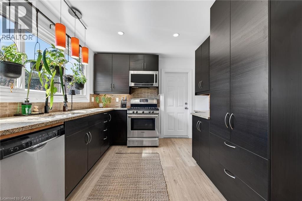 Kitchen with stainless steel appliances, light wood-style floors, light stone countertops, backsplash, and modern cabinets - 844 Upper Wellington Street, Hamilton, ON - Indoor Photo Showing Kitchen