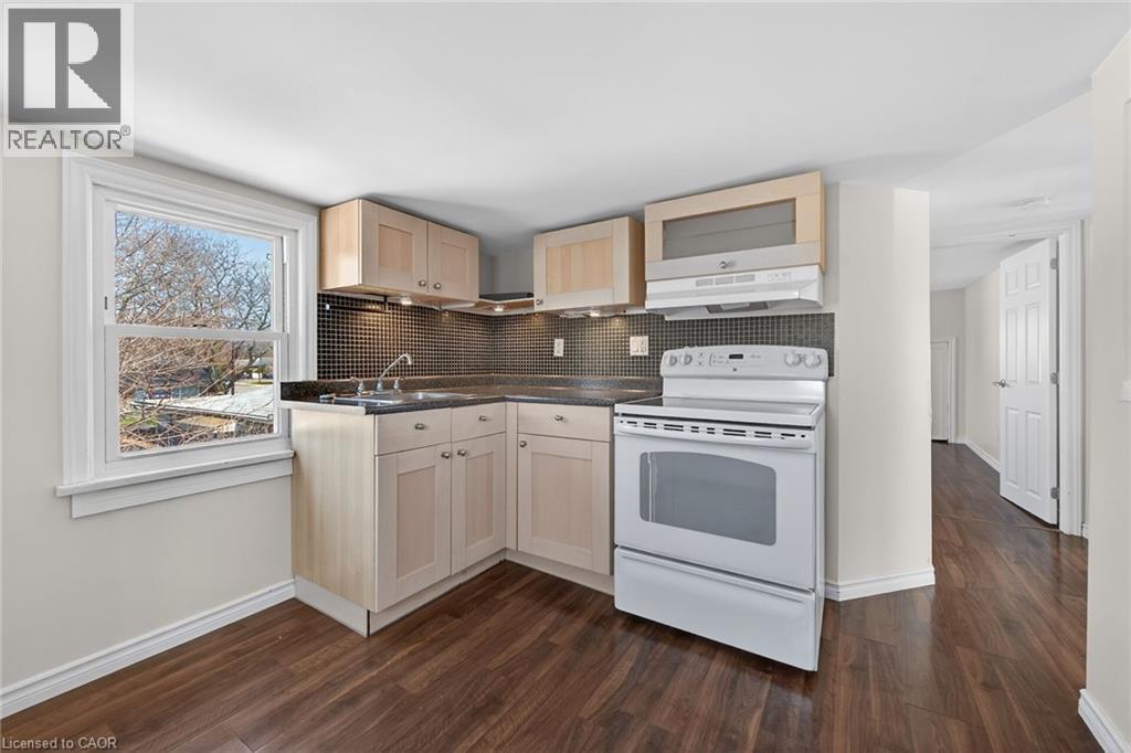 Kitchen featuring white appliances, dark countertops, decorative backsplash, dark wood-style flooring, and light wood finish cabinets - 844 Upper Wellington Street, Hamilton, ON - Indoor Photo Showing Laundry Room