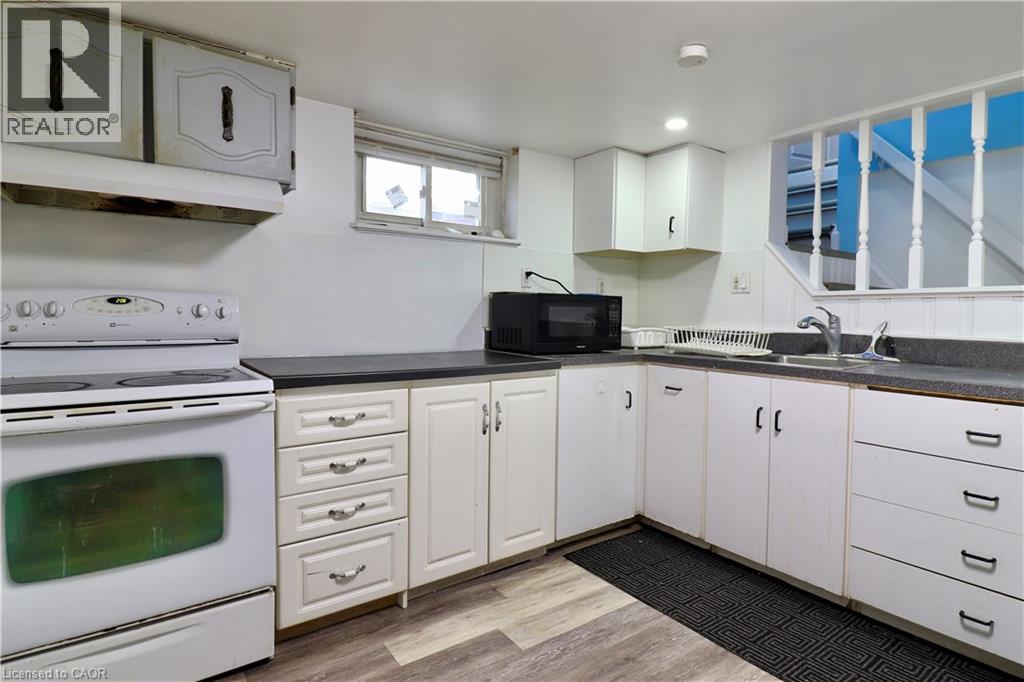 Kitchen in basement with white range with electric stovetop, dark countertops, black microwave, light wood-style flooring, and recessed lighting - 80 Roseview Avenue, Cambridge, ON - Indoor Photo Showing Kitchen With Double Sink