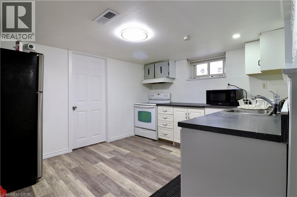 Kitchen in basement featuring electric range, freestanding refrigerator, dark countertops, black microwave, and light wood-type flooring - 80 Roseview Avenue, Cambridge, ON - Indoor Photo Showing Kitchen