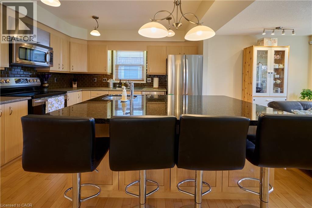 Kitchen featuring stainless steel appliances, light wood finished floors, pendant lighting, dark stone countertops, and backsplash - 126 Snowdrop Crescent, Kitchener, ON - Indoor Photo Showing Kitchen With Stainless Steel Kitchen