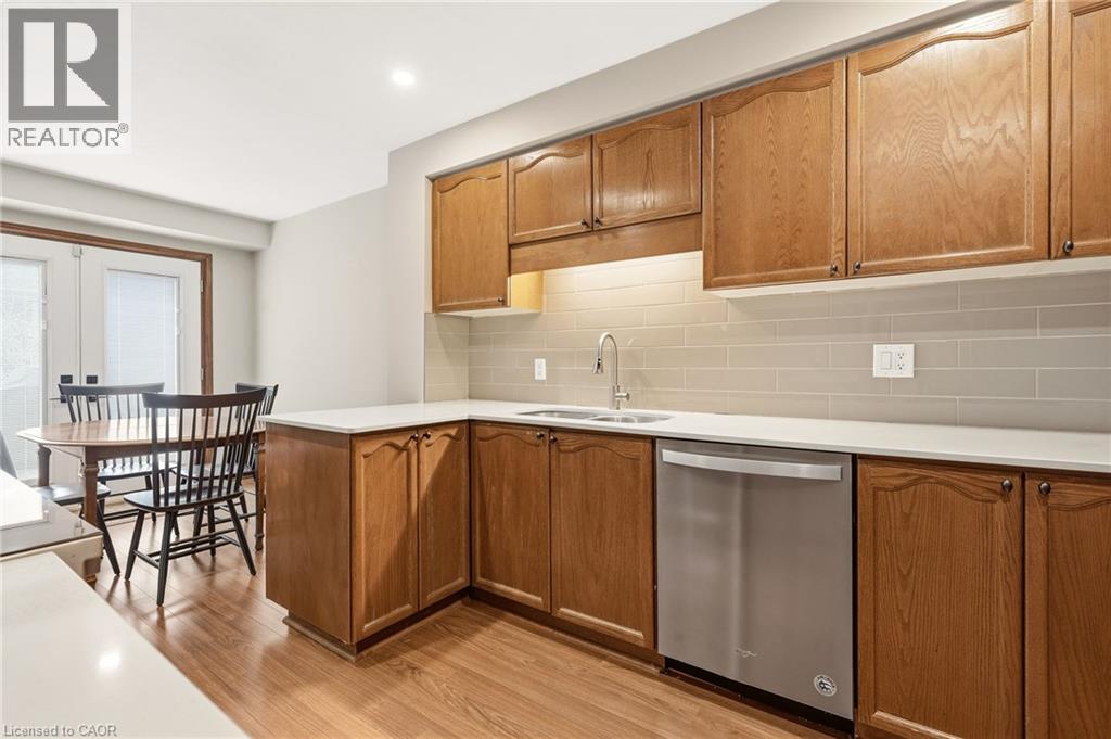 The kitchen features wood cabinetry, light-colored countertops, a stainless steel dishwasher, and a tile backsplash - 1 Tomahawk Drive, Grimsby, ON - Indoor Photo Showing Kitchen With Double Sink