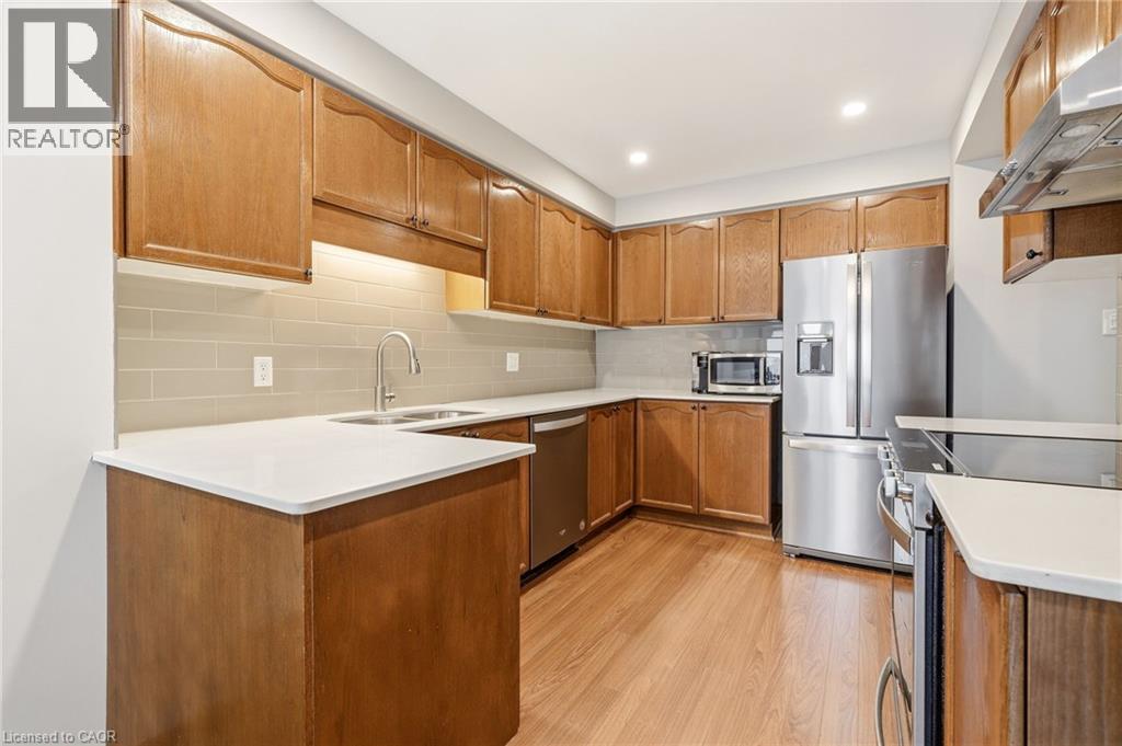 The kitchen features wood cabinetry, light-colored countertops, a tile backsplash, and stainless steel appliances - 1 Tomahawk Drive, Grimsby, ON - Indoor Photo Showing Kitchen With Stainless Steel Kitchen With Double Sink