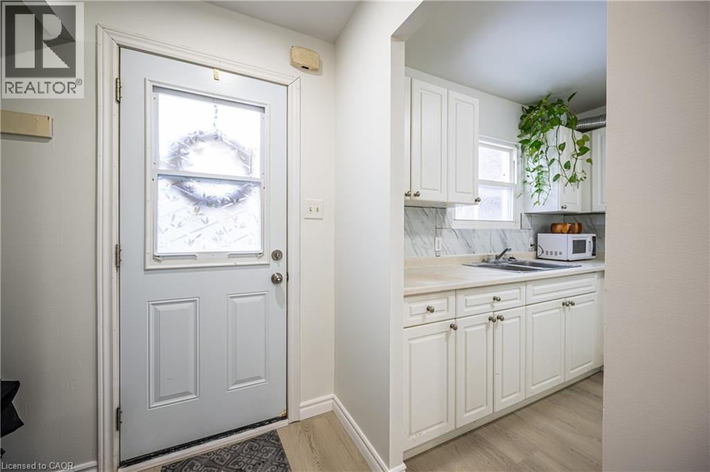 The entrance features a door with a decorative glass insert, leading directly into a kitchen area with white cabinetry, a sink, and a window - 212 Westcourt Place, Waterloo, ON - Indoor