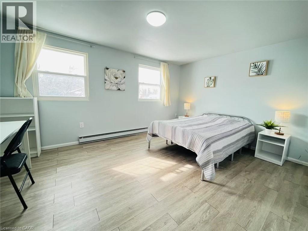 This room features light-colored plank flooring, light blue walls, and two windows with curtains - 212 Westcourt Place, Waterloo, ON - Indoor Photo Showing Bedroom