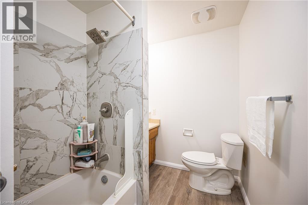 This bathroom features a bathtub and shower combination with white and gray marbled tile surround, a built-in shower caddy, and a shower head with a rain shower feature - 212 Westcourt Place, Waterloo, ON - Indoor Photo Showing Bathroom