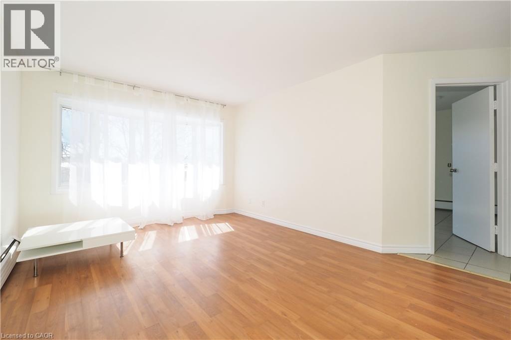 This room features light hardwood flooring, a window with sheer white curtains, and a white baseboard heater - 24 Austin Drive, Waterloo, ON - Indoor Photo Showing Other Room