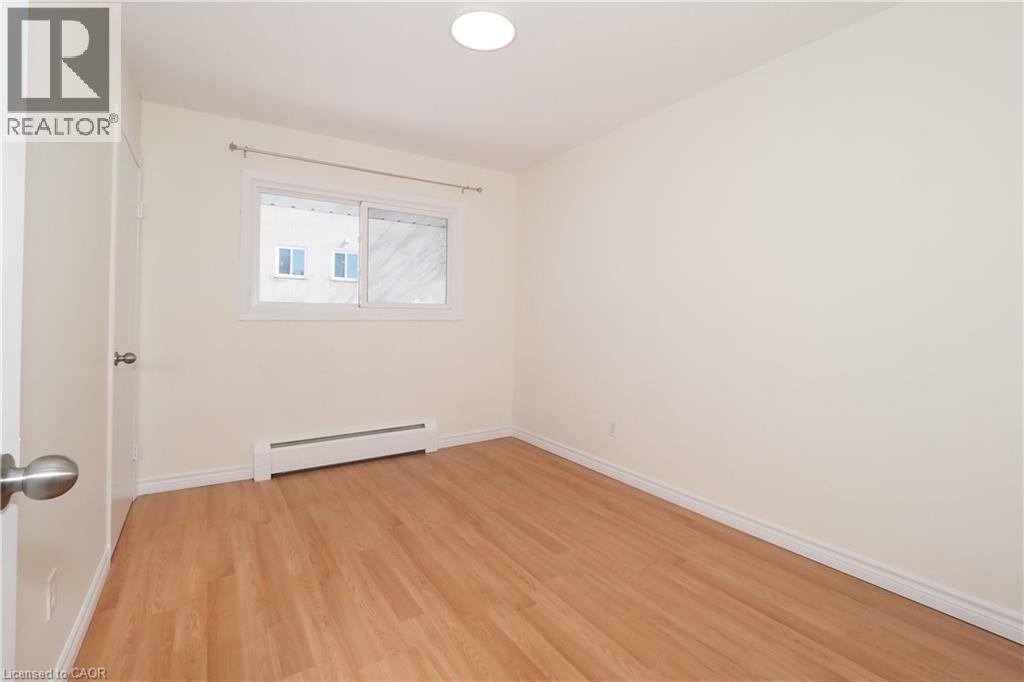 Bright room featuring light-toned hardwood flooring, a window with a curtain rod, and a baseboard heater - 24 Austin Drive, Waterloo, ON - Indoor Photo Showing Other Room