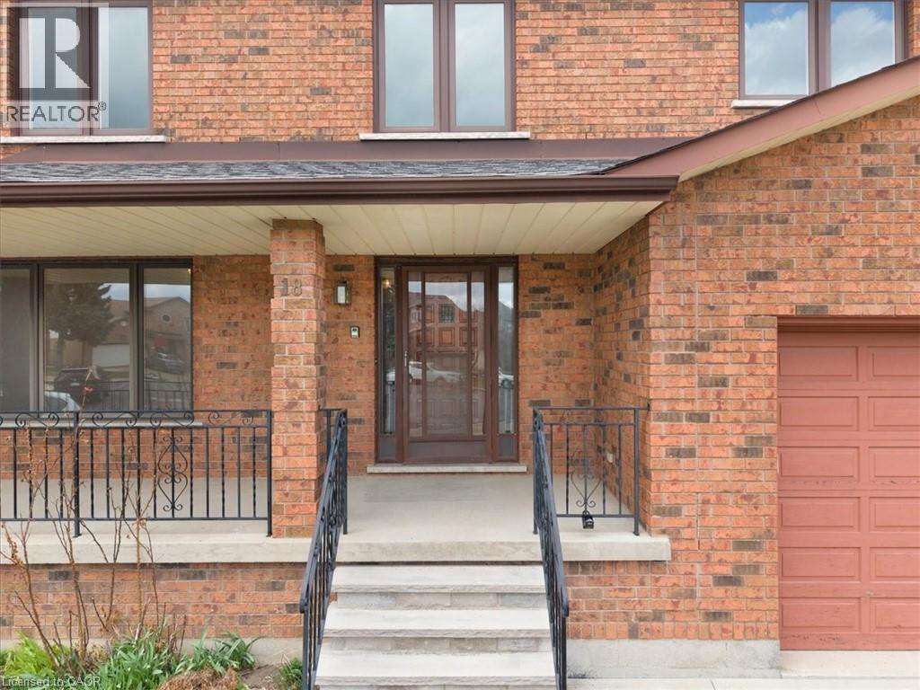 The property features a brick exterior, a covered front porch with decorative iron railings, and a garage with a panelled door - 18 Marcel Place, Hamilton, ON - Outdoor With Exterior