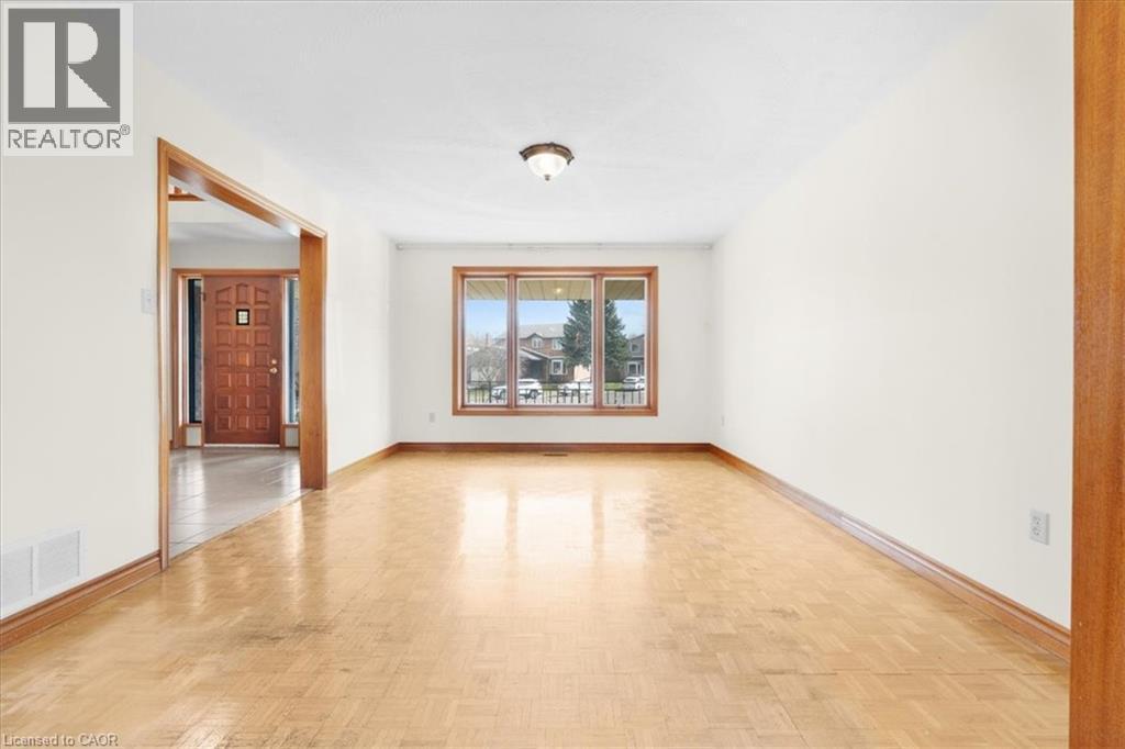 This inviting room features light-toned hardwood flooring, a bright window offering views of the neighborhood, and an entrance with a wooden door - 18 Marcel Place, Hamilton, ON - Indoor