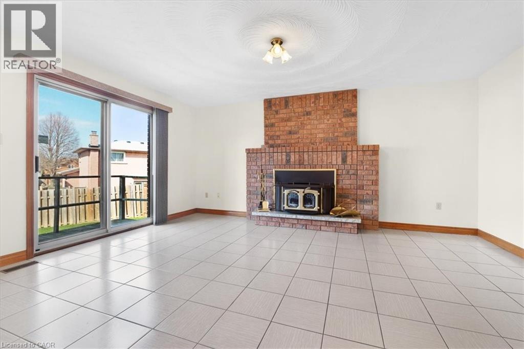 The living area features a brick fireplace with a wood-burning insert and a sliding glass door providing external access - 18 Marcel Place, Hamilton, ON - Indoor Photo Showing Living Room With Fireplace