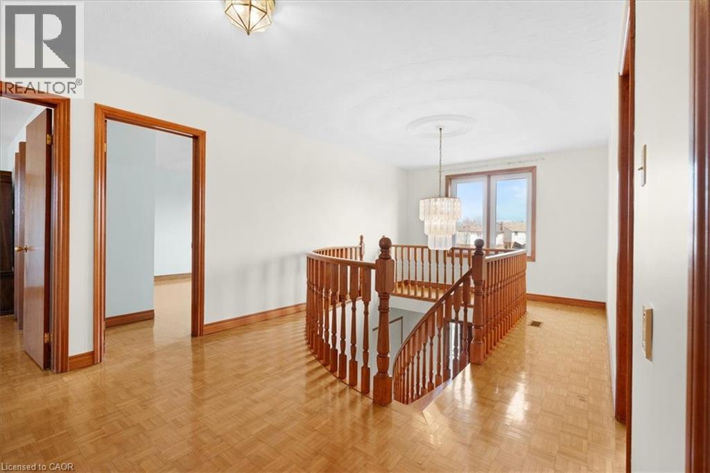 The property features parquet flooring, a wooden staircase with a matching railing, and a chandelier with a decorative ceiling medallion - 18 Marcel Place, Hamilton, ON - Indoor Photo Showing Other Room