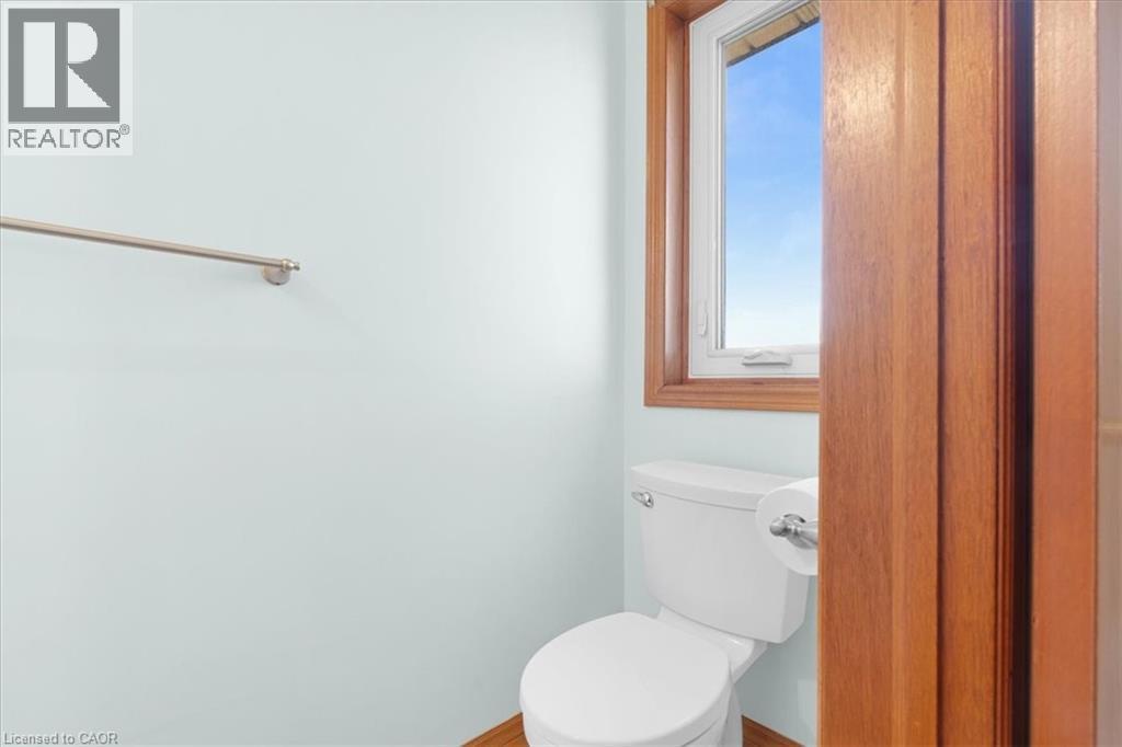 A well-appointed bathroom featuring a window with wood trim, a white toilet, and light-colored walls - 18 Marcel Place, Hamilton, ON - Indoor Photo Showing Bathroom