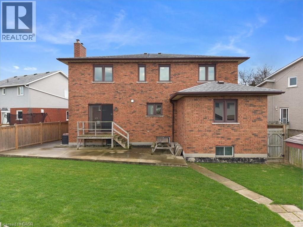 The property features a brick exterior with multiple windows and a chimney, complemented by a well-maintained lawn and a patio area - 18 Marcel Place, Hamilton, ON - Outdoor With Deck Patio Veranda With Exterior