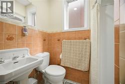Bathroom featuring a white pedestal sink, toilet, and a tiled shower area with a shower curtain -