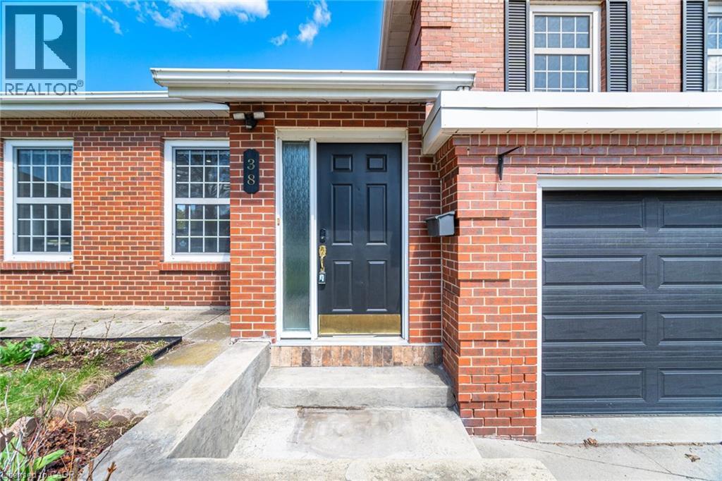 The property features a brick exterior, a dark front door with a sidelight, and a gray garage door - 38 Leclaire Street, Hamilton, ON - Outdoor