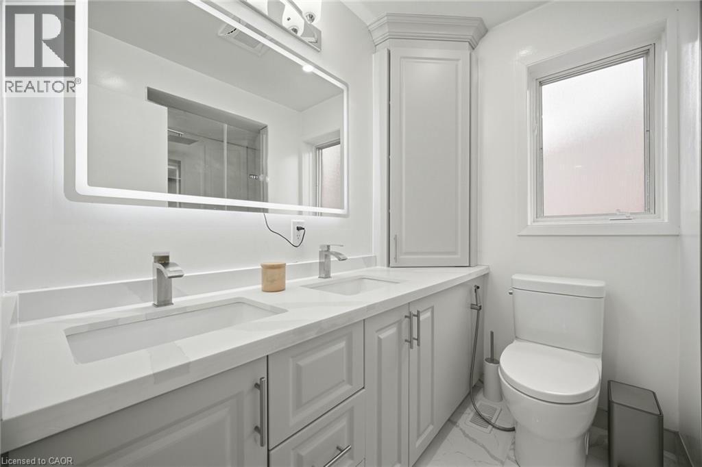 This bathroom features a double vanity with stone countertops and two undermount sinks - 38 Leclaire Street, Hamilton, ON - Indoor Photo Showing Bathroom