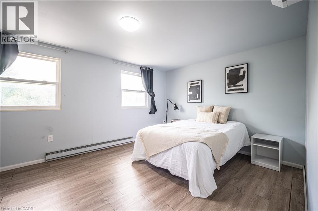 Bedroom featuring wood-finish flooring, two large windows, a flush-mount ceiling light, and baseboard heating - 212 Westcourt Place, Waterloo, ON - Indoor Photo Showing Bedroom