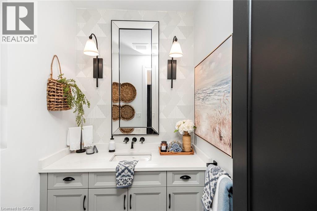 Bathroom vanity featuring light gray cabinetry with black hardware, a white countertop, and an integrated rectangular sink - 253 Central Avenue, Grimsby, ON
