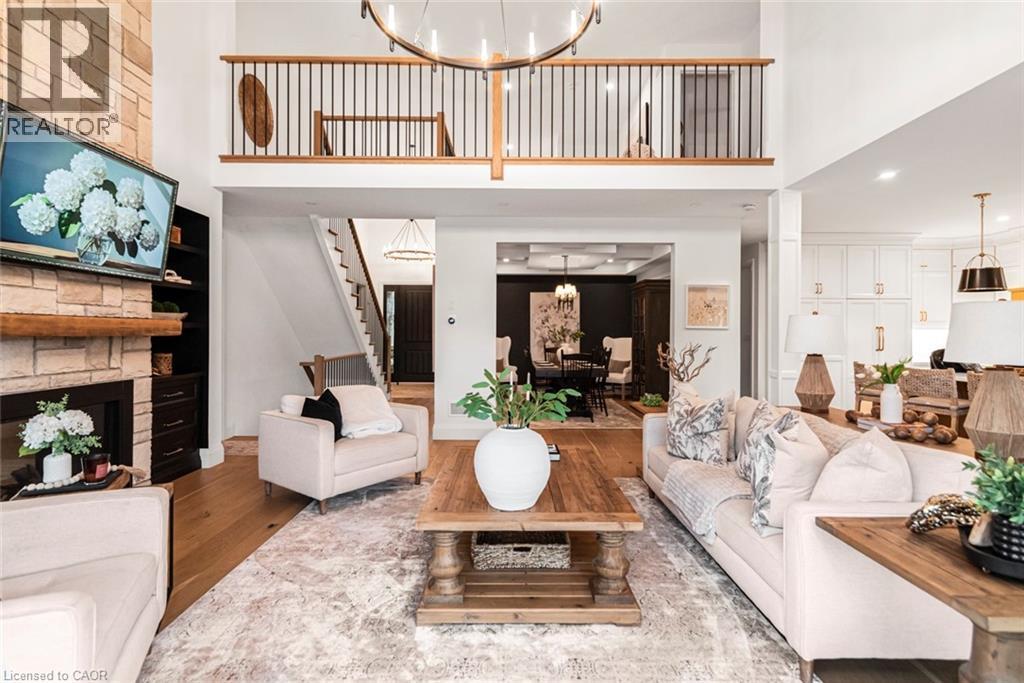 Open-concept living area featuring a two-story ceiling, stone fireplace with wood mantel, a second-story balcony with metal balusters, hardwood flooring, and recessed lighting - 253 Central Avenue, Grimsby, ON