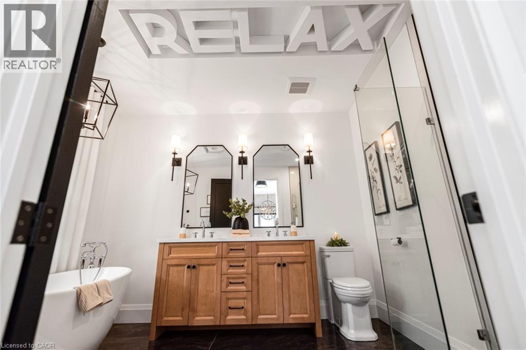 Contemporary bathroom featuring a freestanding soaking tub, wood-finish double vanity with stone countertop, frameless glass shower enclosure, and dark tile flooring - 253 Central Avenue, Grimsby, ON